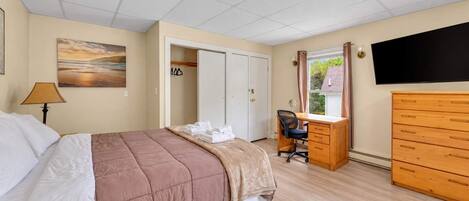 A bedroom with a bed, desk, dresser, and a TV.