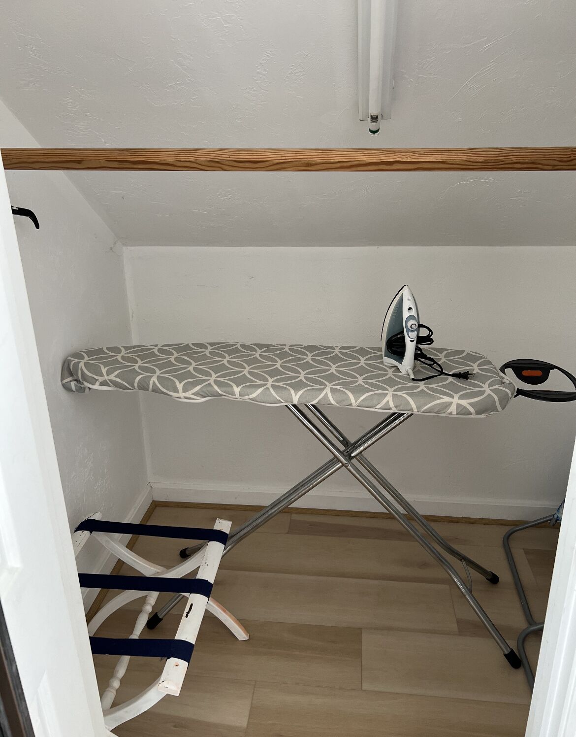A compact, wooden-framed ironing station with a patterned ironing board, an iron, and a small stool.