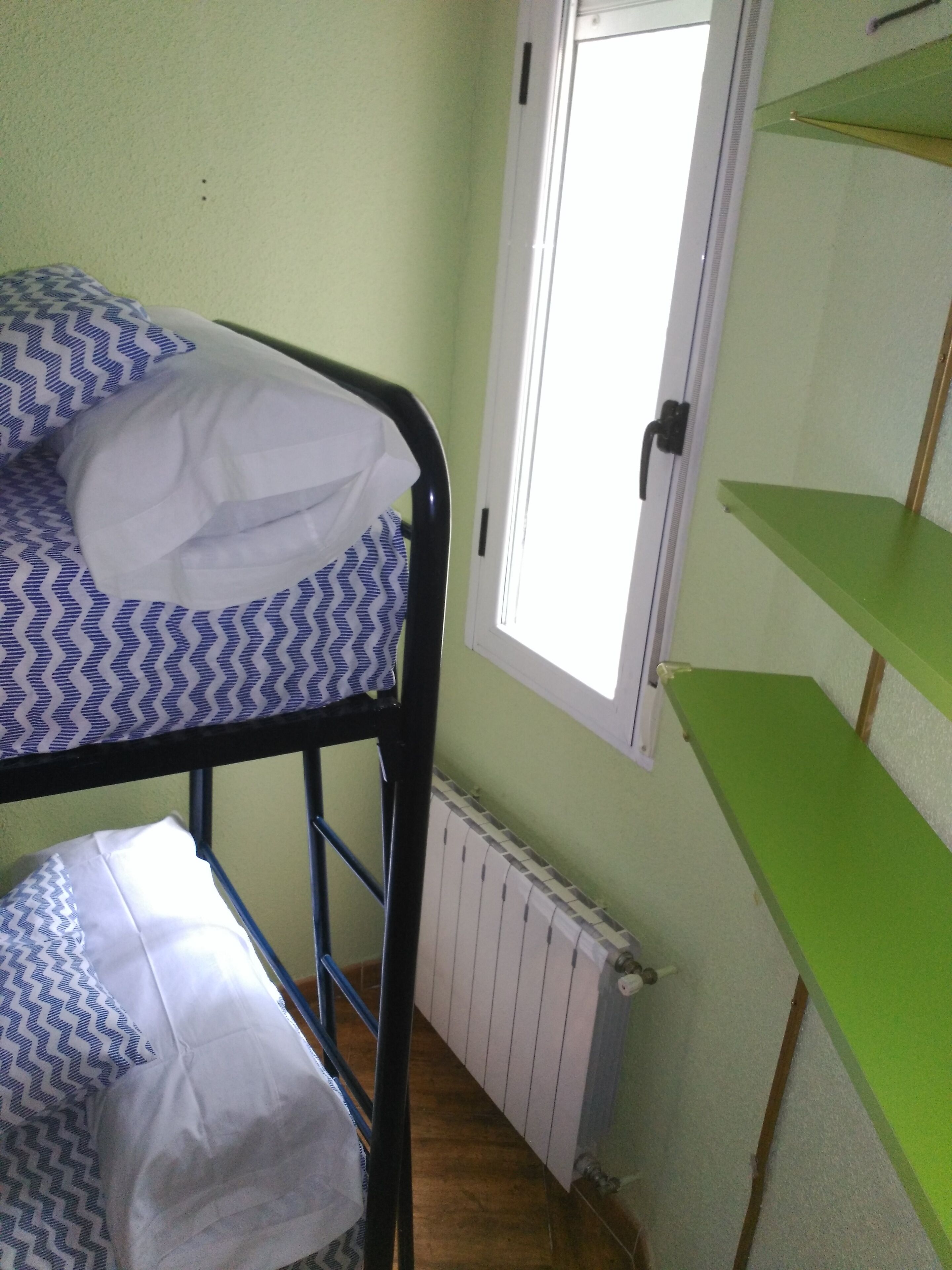 Een stapelbed met beddengoed met patroon, een groen schap en een raam met deur.