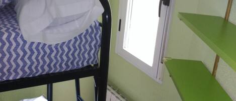 Een stapelbed met beddengoed met patroon, een groen schap en een raam met deur.