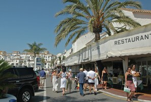 A street with people walking, palm trees, and a restaurant named "RESTAURANT ANTONIO". - Beachside Puerto Banus Stunning Apartment 212 (Marbella)