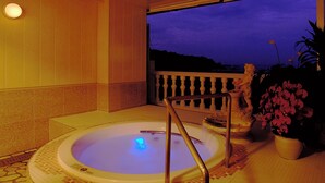 Uma banheira de hidromassagem com vista para o céu noturno, guarda-corpo de varanda e um vaso de plantas.