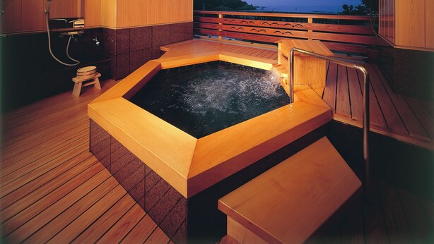Uma área de spa em madeira com hidromassagem, um deck de madeira e vista para o mar.