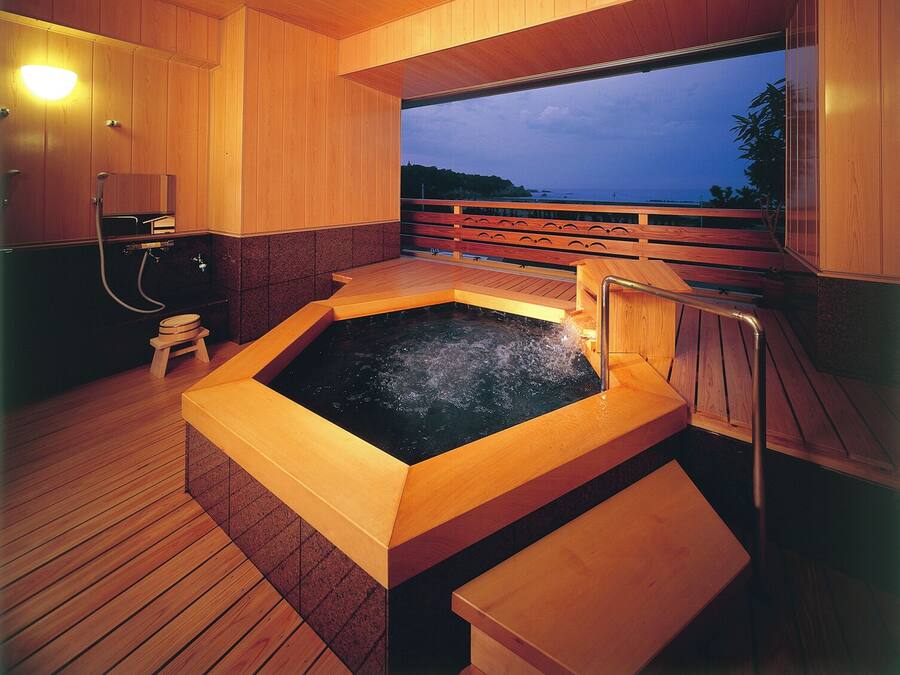 A wooden spa area with a hot tub, wooden deck, and a view of the sea.