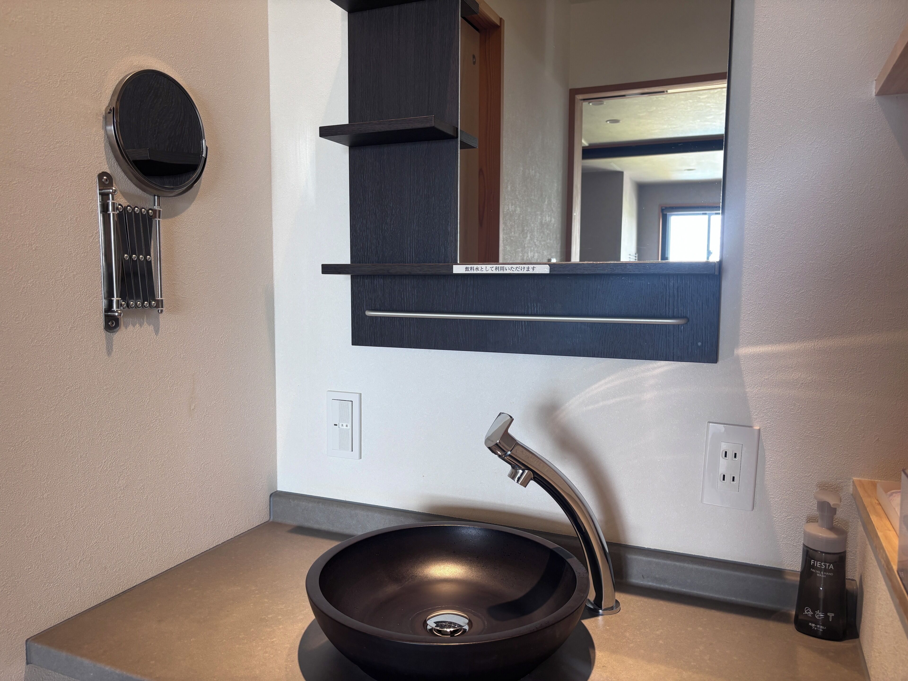 Un baño moderno con un lavamanos tipo recipiente negro, un espejo redondo y un perchero.