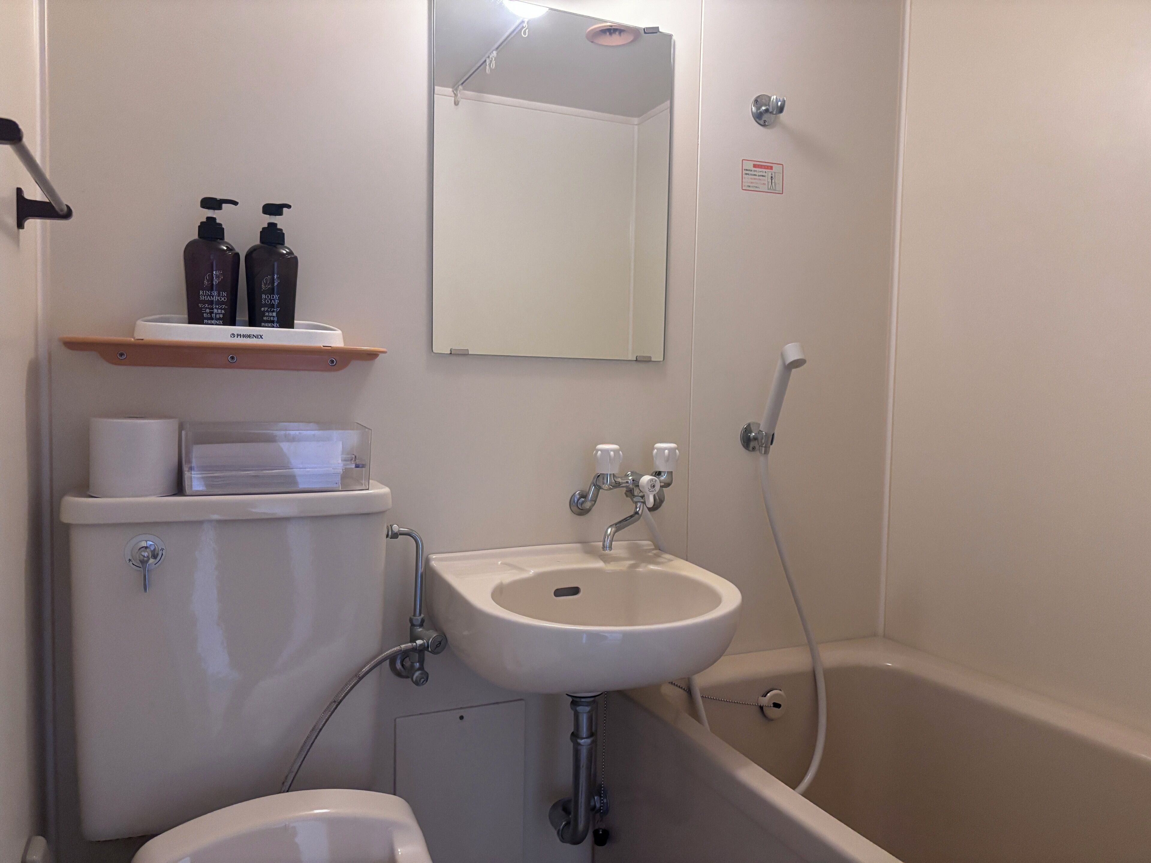 A bathroom with a toilet, sink, and bathtub. There are toiletries on a shelf, and a mirror above the sink.