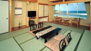 Quarto japonês tradicional com tatames, uma mesa baixa com almofadas, uma televisão e vista para o oceano.
