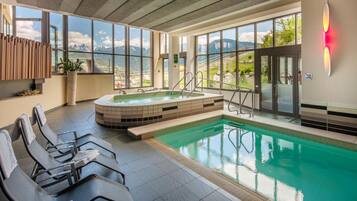 Area piscina interna moderna con vasca idromassaggio, posti a sedere e ampie finestre con vista sulle montagne.