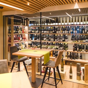 A wine cellar with shelves of wine bottles, a table with chairs, and a wooden ceiling. - Feldthurnerhof Panorama Wellness Hotel (Velturno)