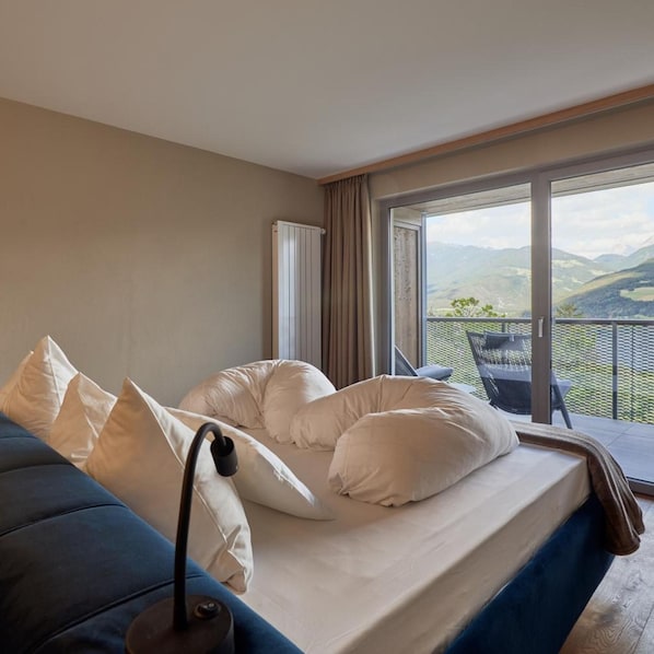 Een slaapkamer met een bed, kussens, een bedlampje en uitzicht op een balkon met een stoel.