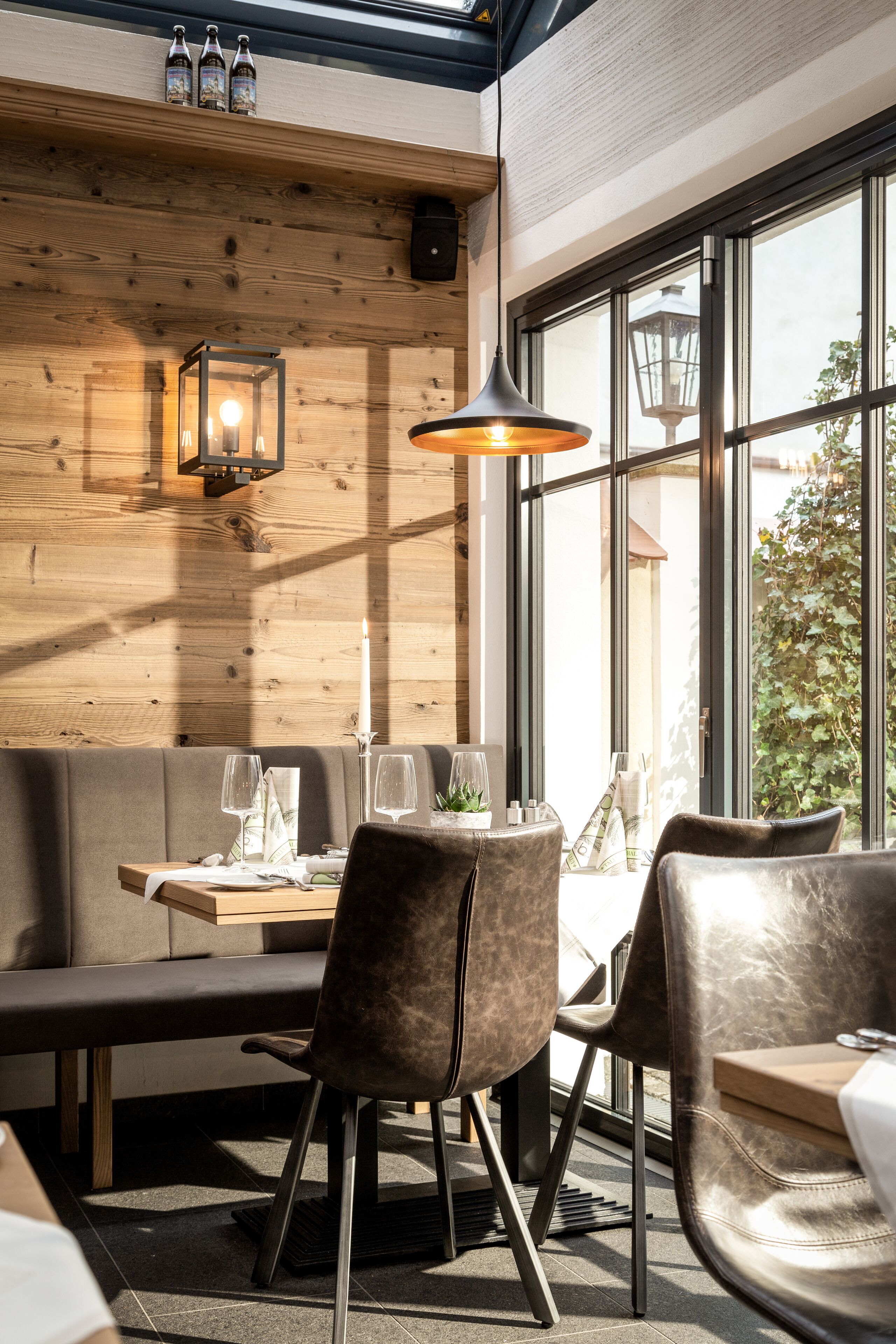 A cozy restaurant interior with wooden walls, a large window, and a table set for two.