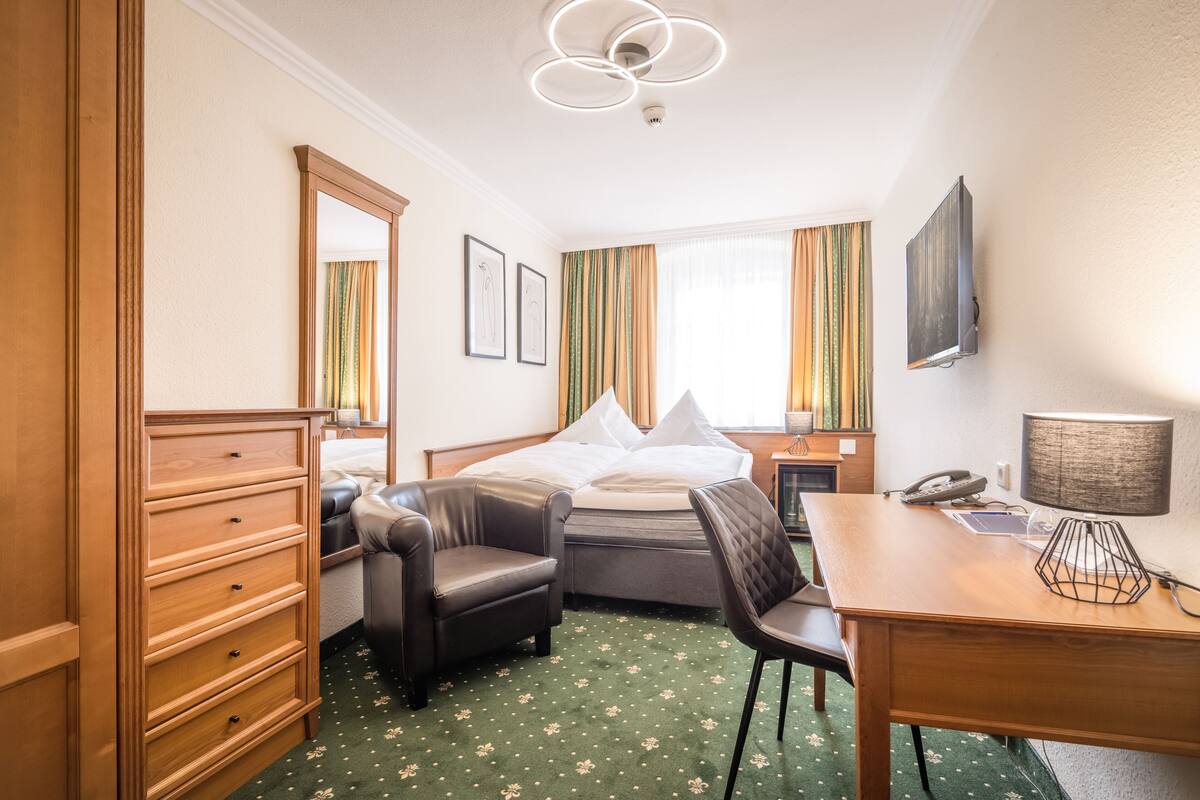 Une chambre d’hôtel comprenant un lit, un bureau, une chaise, une commode et un miroir.