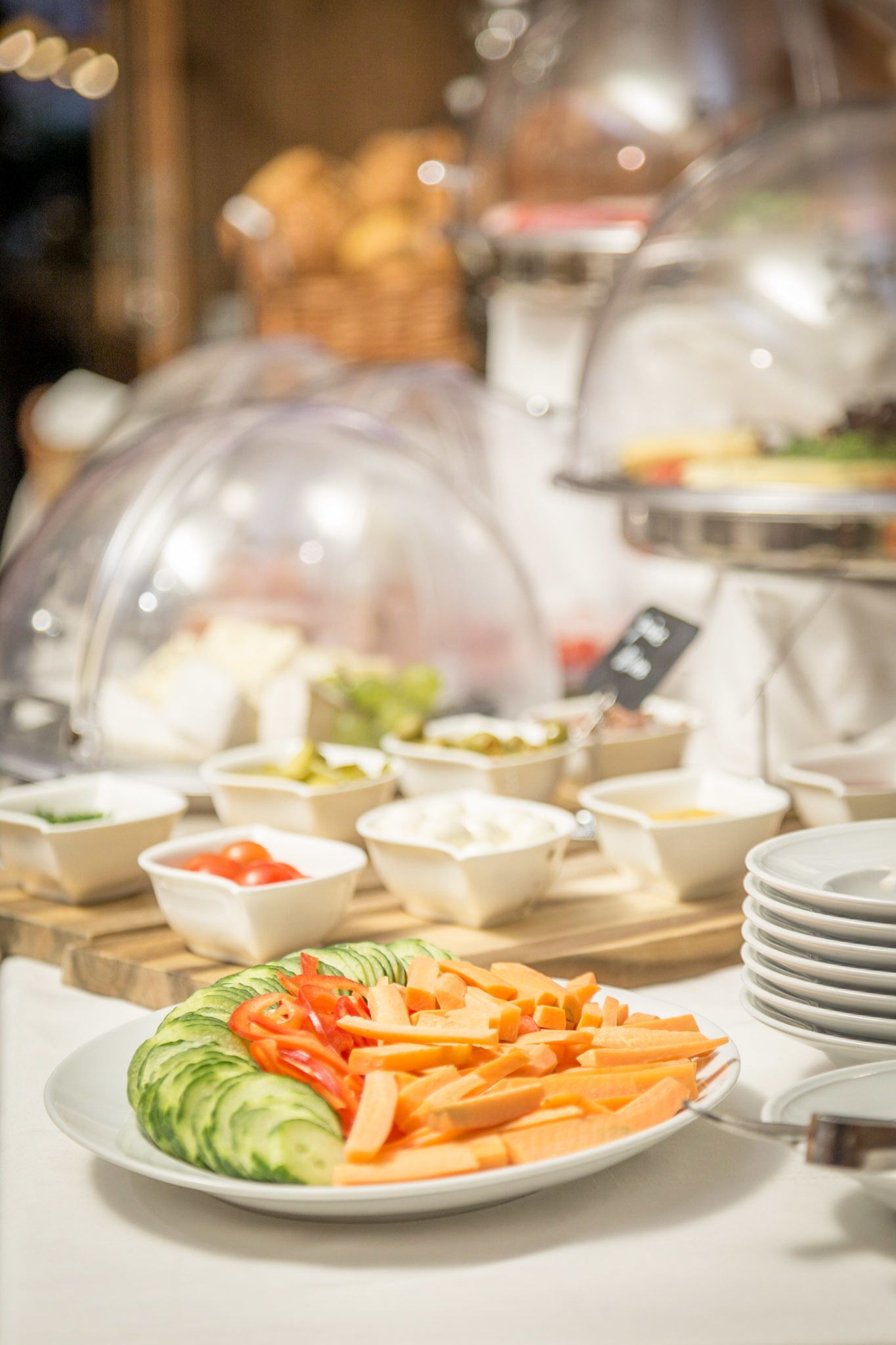 A buffet with various food items under glass domes, including sliced vegetables and bowls of dips.