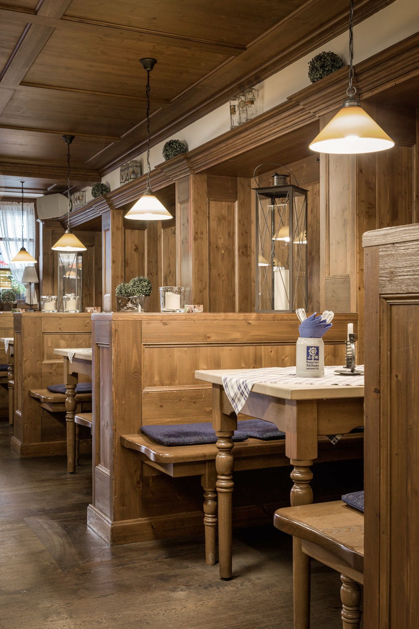 Een restaurantinterieur met houten zithoeken, hanglampen en een tafel met menukaart houder.