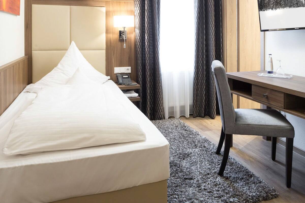 Une chambre d’hôtel avec un lit, un bureau, une chaise, une lampe et un tableau au mur.