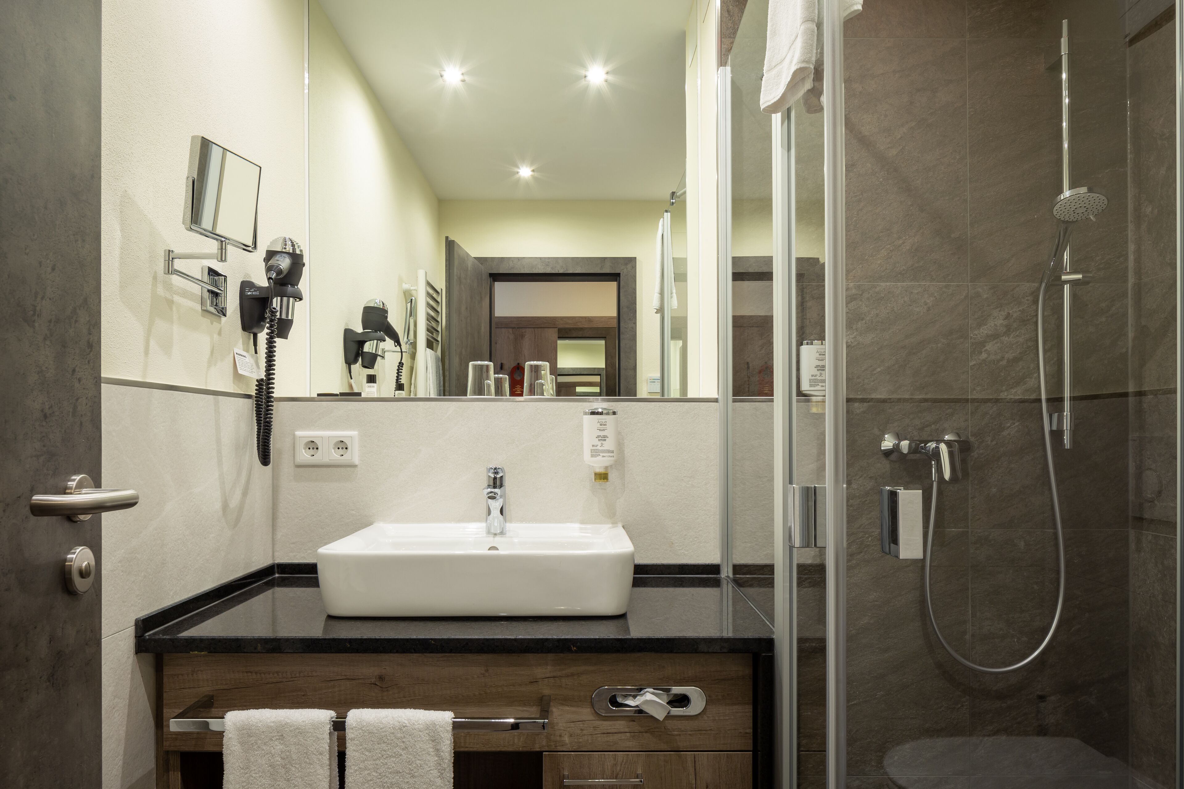 A modern bathroom with a large mirror, a sink, and a shower.