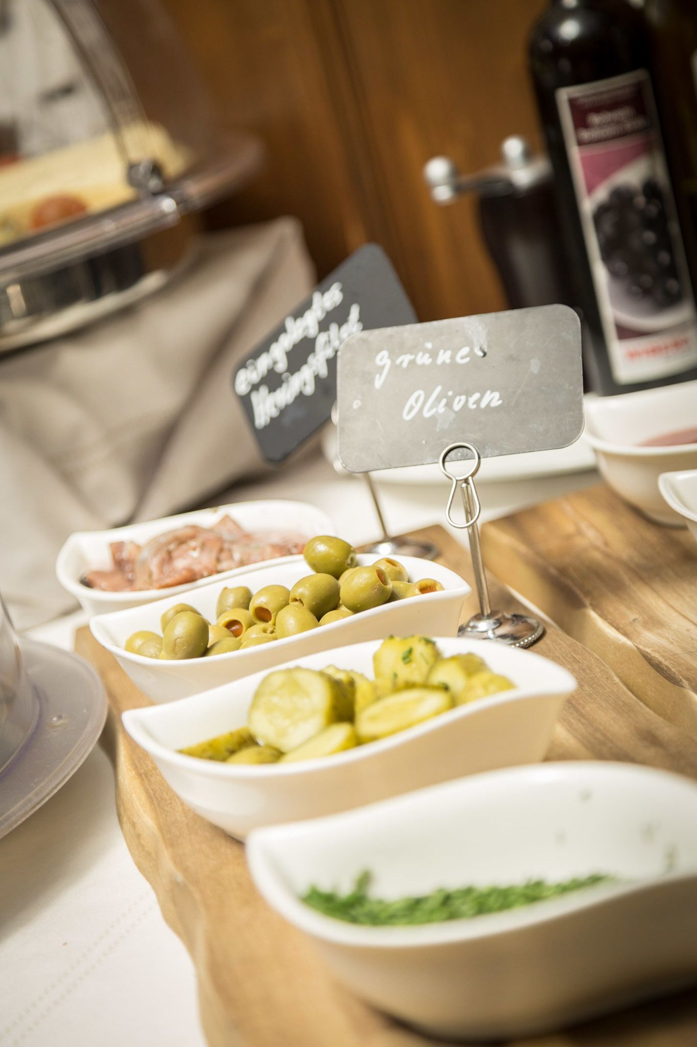 A buffet table with various food items including olives, pickles, and a sign indicating 'grüne Oliven' (green olives).