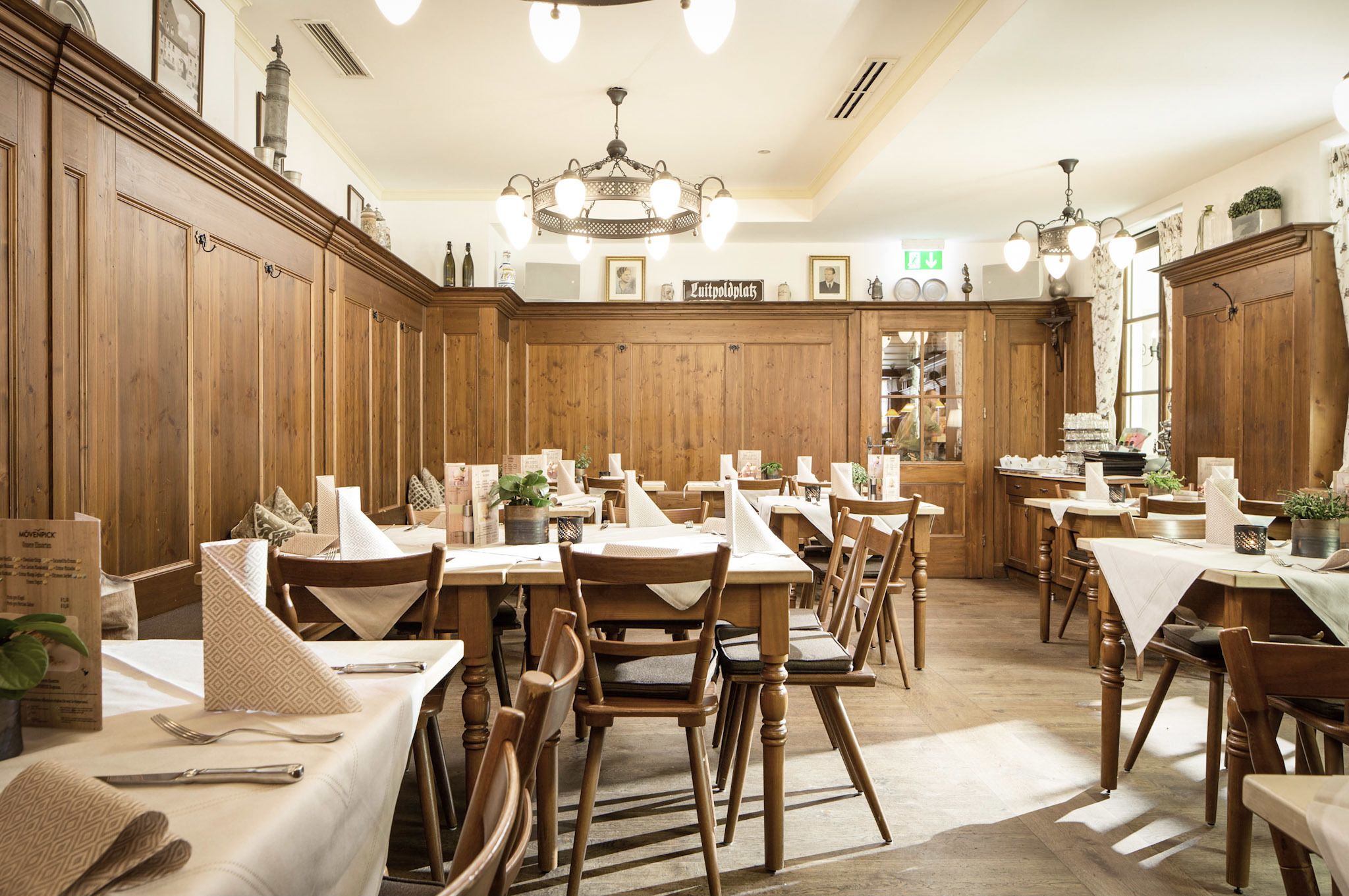 Un restaurant avec des boiseries, de nombreuses tables recouvertes de nappes blanches et un lustre.