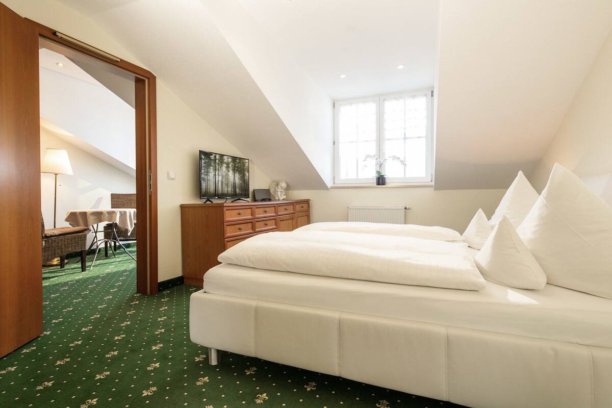 Une chambre à coucher comprenant un lit, une commode, un bureau, une chaise, une lampe, une fenêtre et un radiateur.