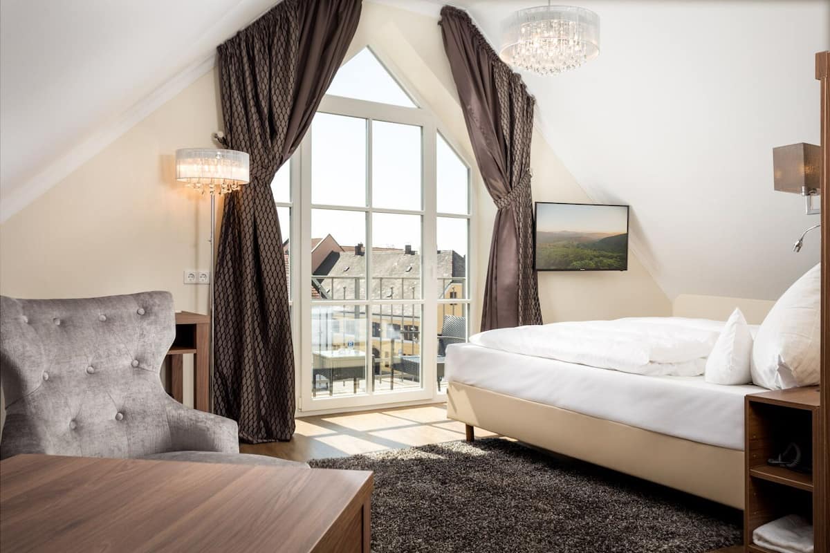Une chambre à coucher avec un lit, une chaise, une table et une vue sur les bâtiments, visible à travers une grande fenêtre.