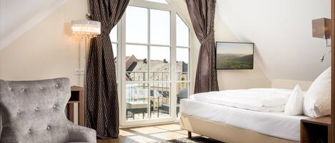 A bedroom with a bed, a chair, a table, and a view of buildings through a large window.
