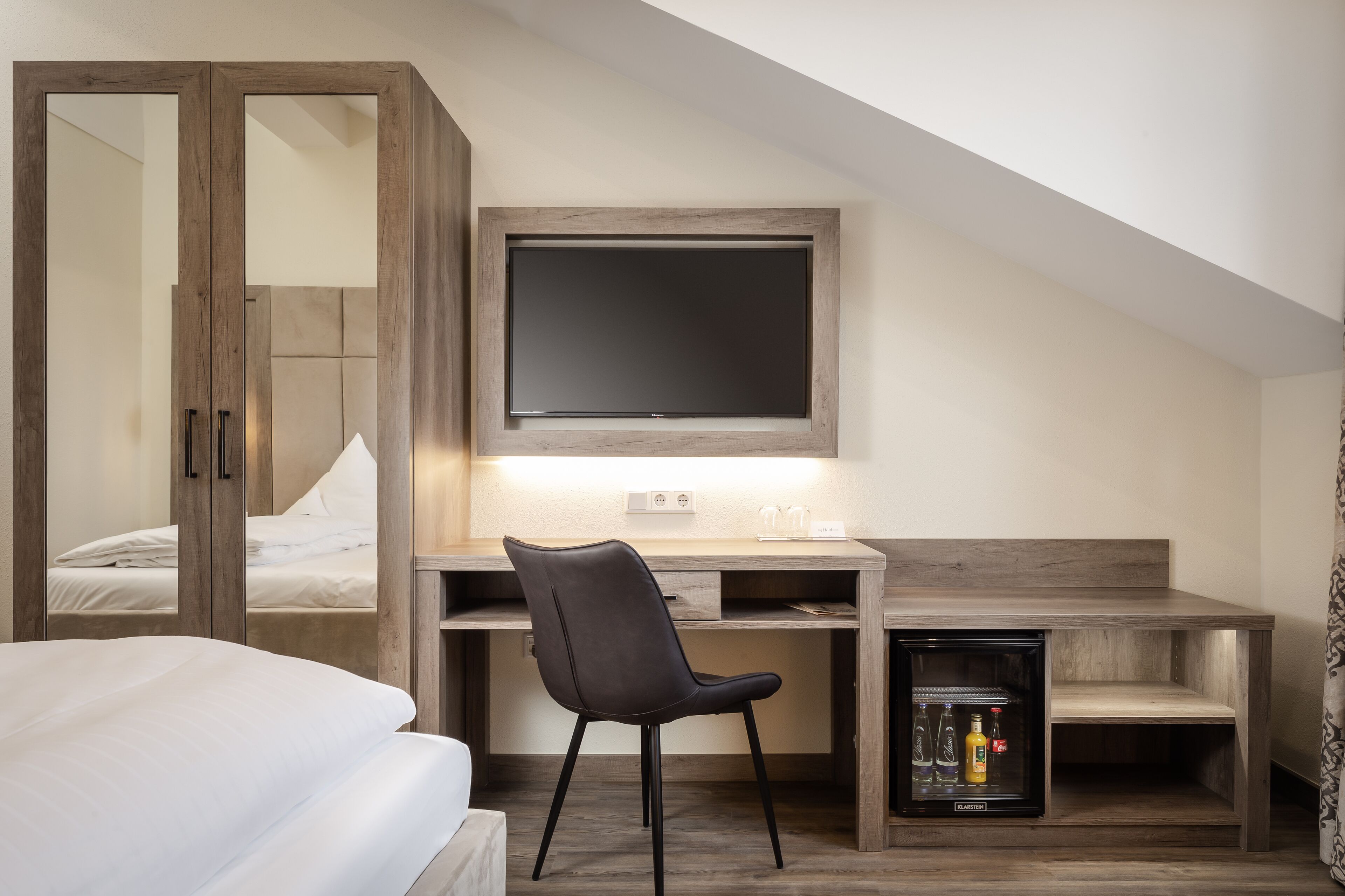 Un dormitorio con cama, escritorio con silla, televisor y minibar.