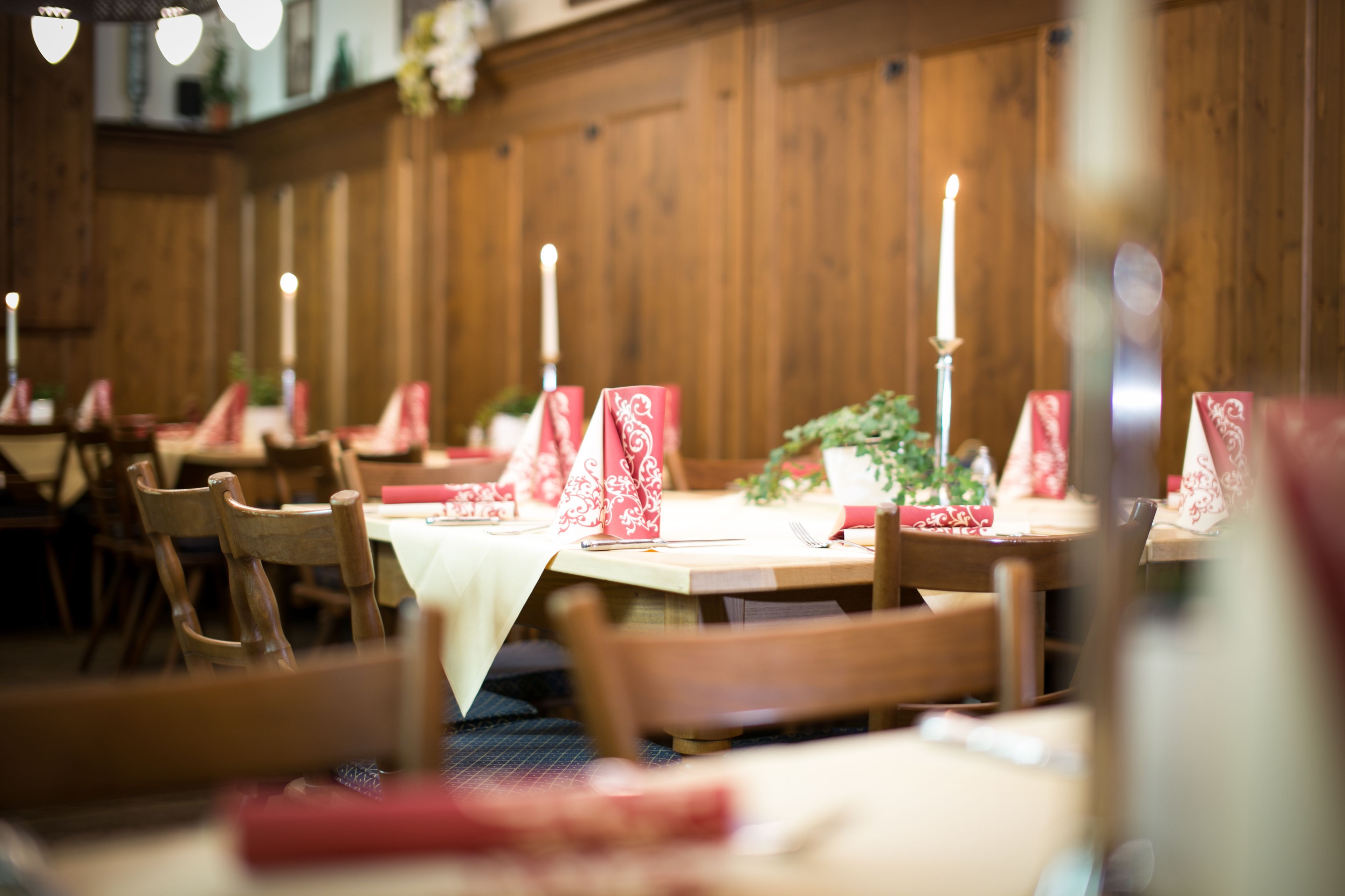 A restaurant with wooden walls and tables set with red napkins and candles.