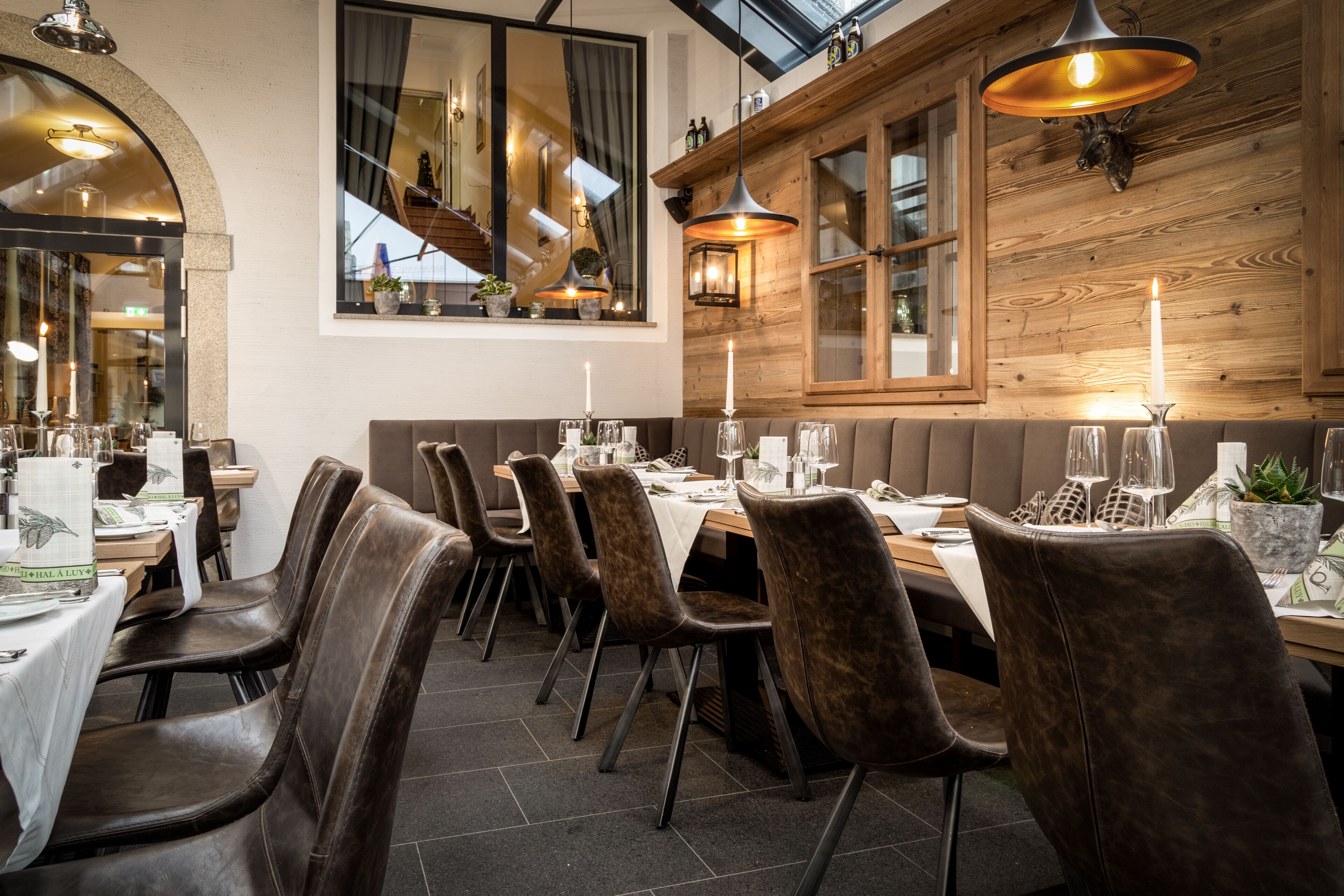 A restaurant with a long wooden bench, dark leather chairs, and a high ceiling with skylights.