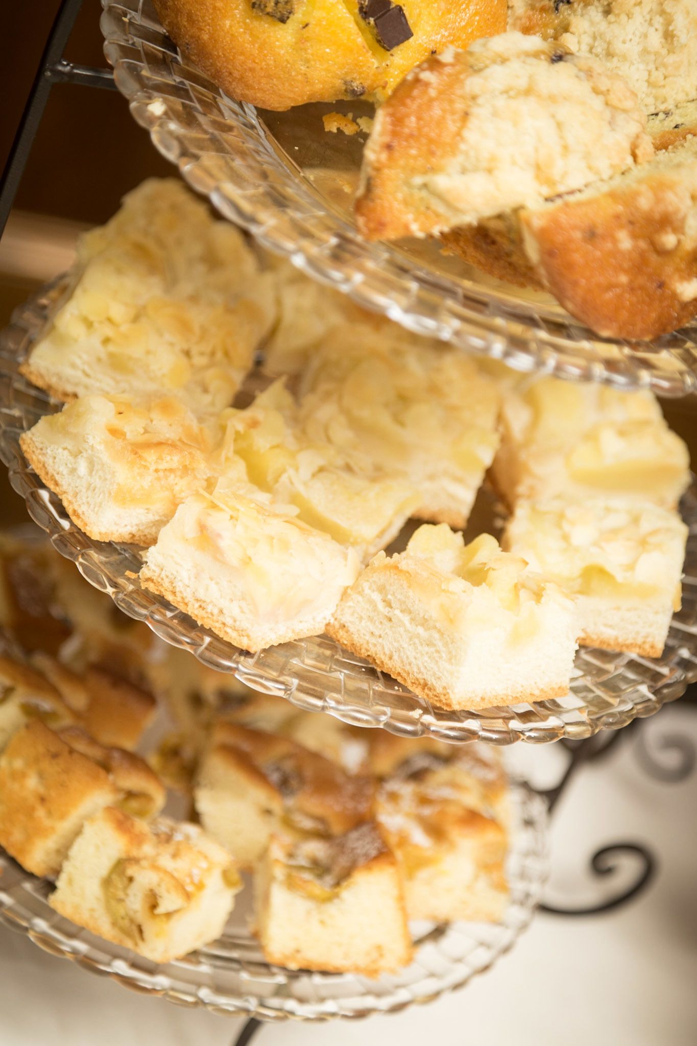 A multi-tiered glass stand displaying various types of bread and pastries.