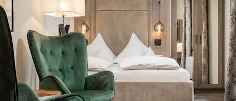 A hotel room with a bed, a green armchair, a lamp, and a mirror.