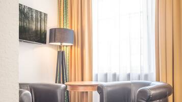 A room with two leather armchairs, a round wooden table, a floor lamp, and a painting on the wall.