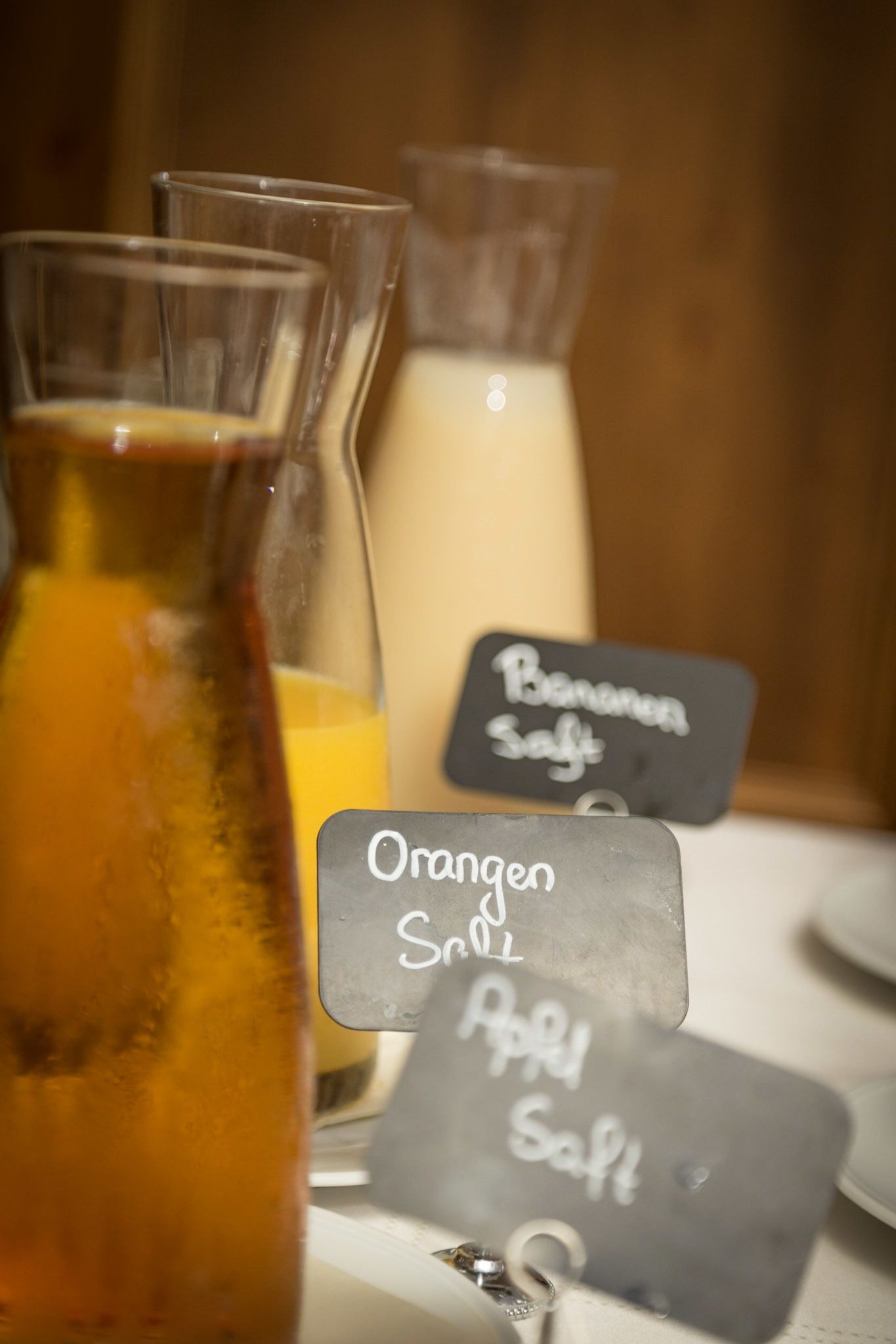 Une table sur laquelle se trouvent deux bouteilles en verre, l’une portant l’étiquette « Orangen Saft » et l’autre « Bananen Saft », ce qui indique la présence de jus d’orange et de jus de banane.