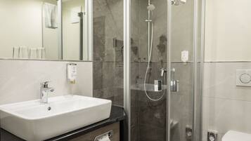 Un baño moderno con ducha de vidrio, un lavamanos blanco y un inodoro.