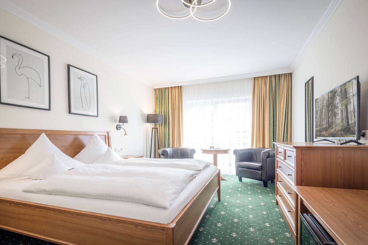 Une chambre d’hôtel avec un lit en bois, deux chaises, un bureau et un téléviseur.