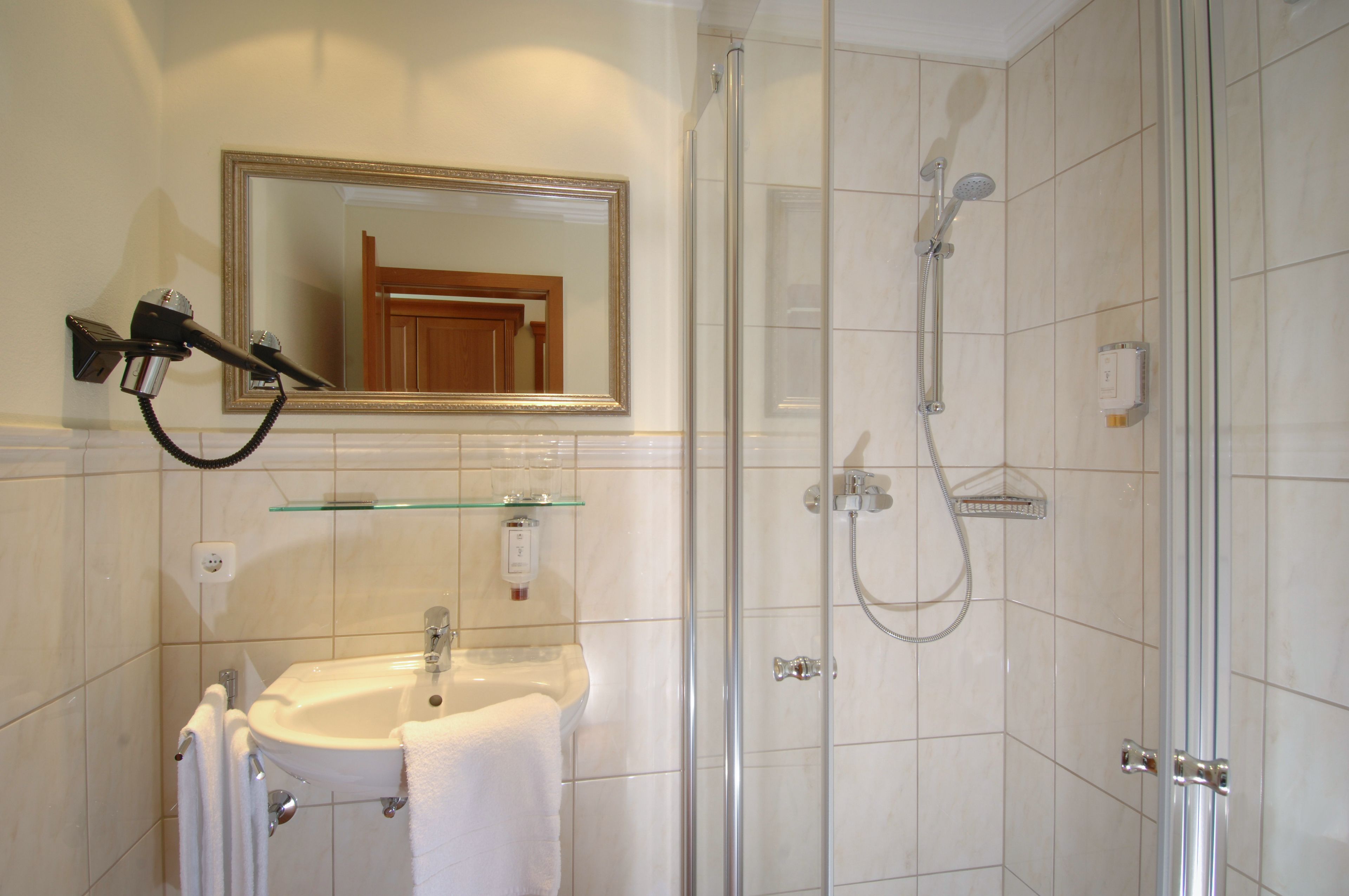 Un baño con cabina de ducha de vidrio, un lavabo con espejo y un secador de pelo montado en la pared.