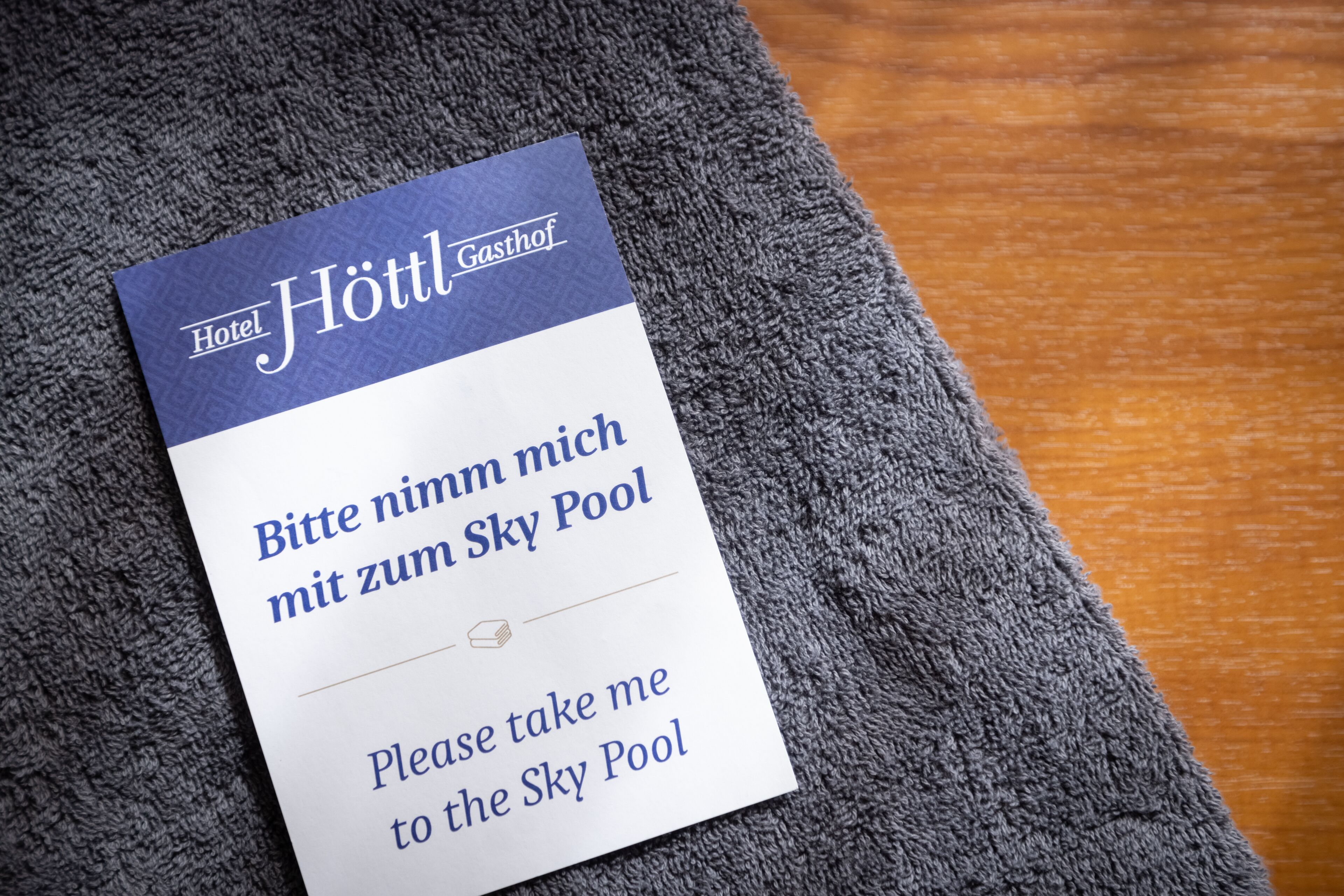 Señal de hotel con el nombre 'Hotel Höttl Gasthof' y un mensaje en alemán e inglés solicitando llevar al huésped a la Piscina Sky.