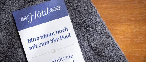 Señal de hotel con el nombre 'Hotel Höttl Gasthof' y un mensaje en alemán e inglés solicitando llevar al huésped a la Piscina Sky.