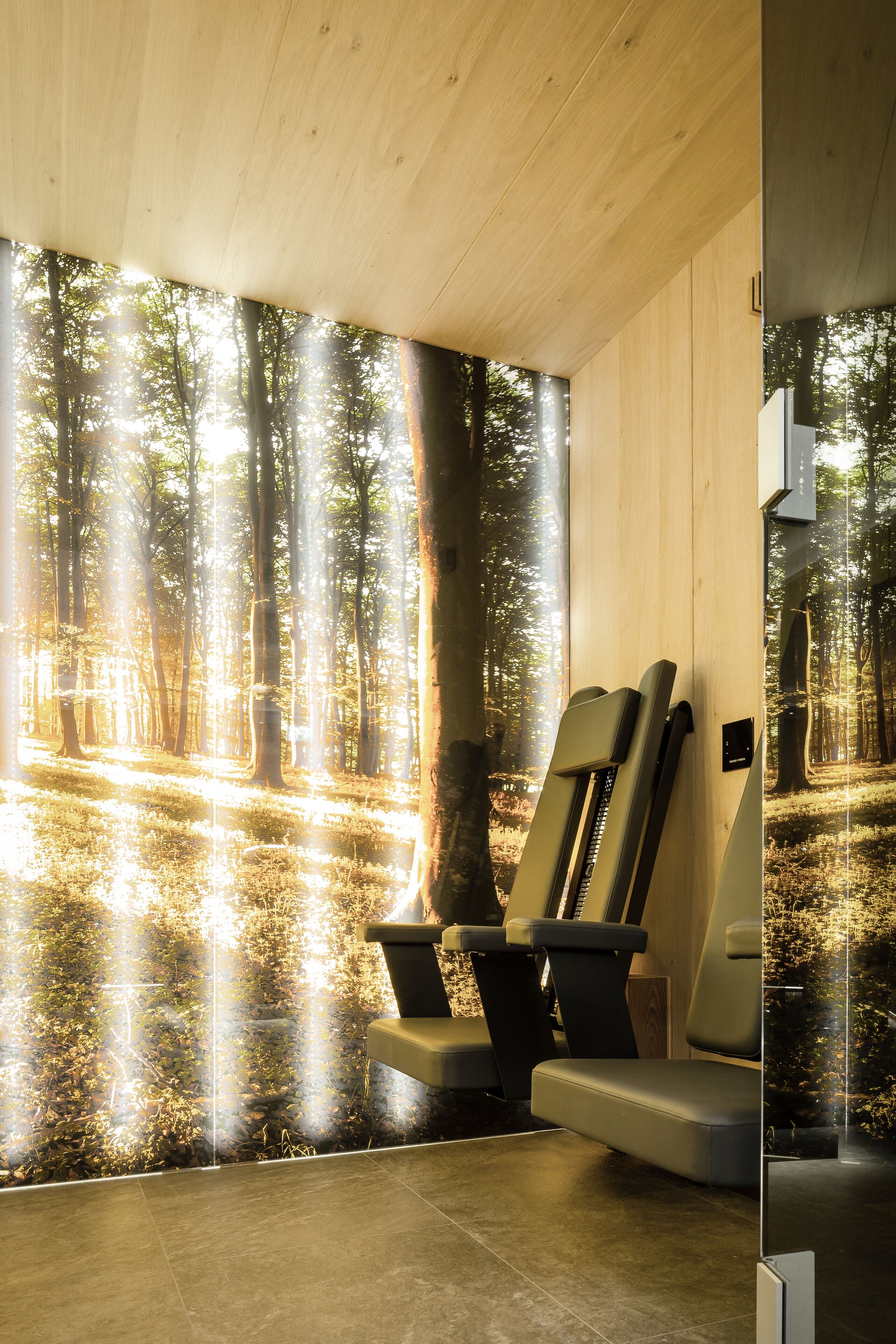 Una habitación con un amplio mural de un bosque, dos sillones de masaje y techo de madera.