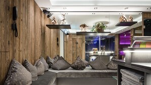 Un moderno vestíbulo de hotel con una pared de madera, una zona de estar con cojines estampados y una recepción con una planta y elementos decorativos.
