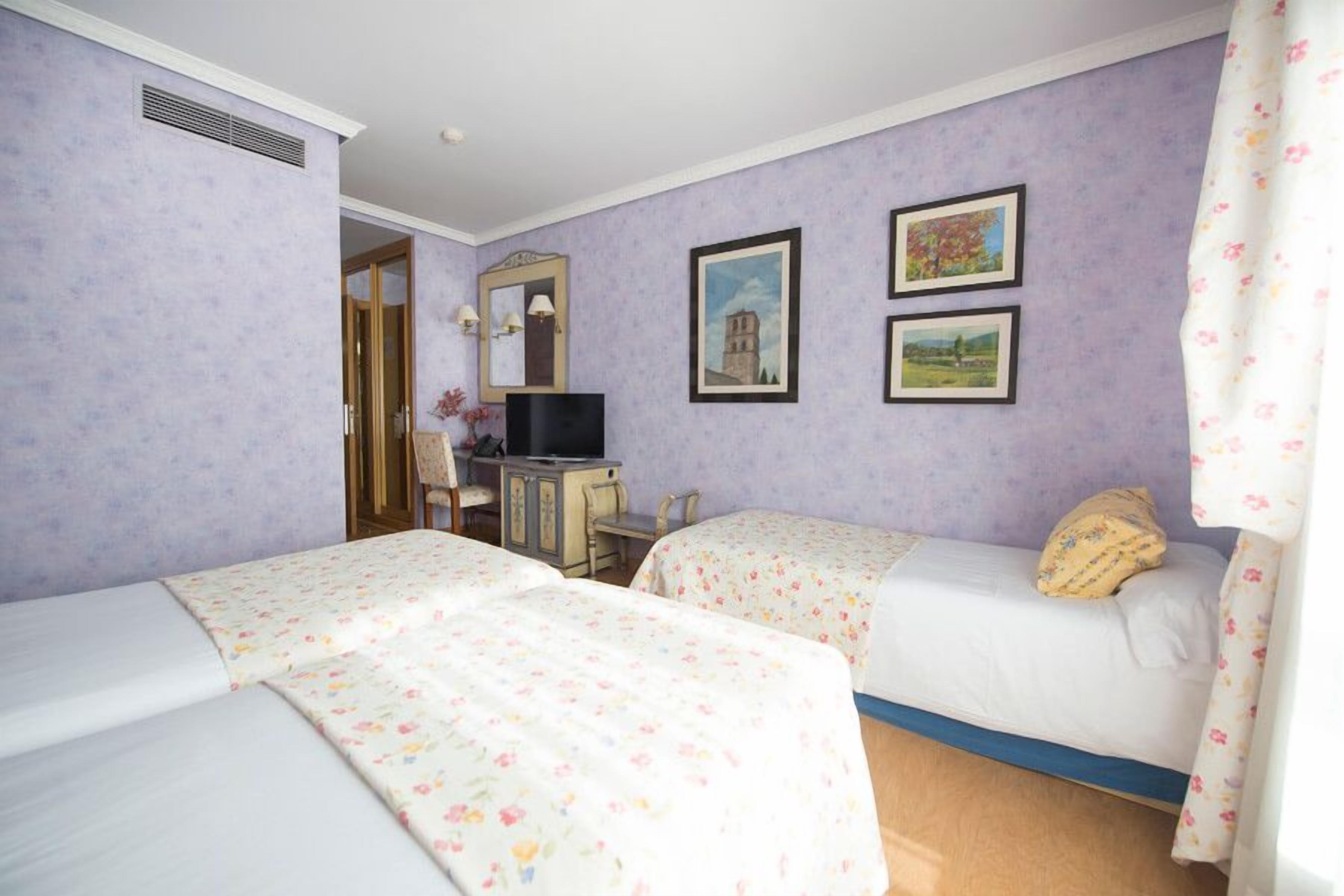 A room with two beds, a desk, a chair, a television, and two framed pictures on the wall.