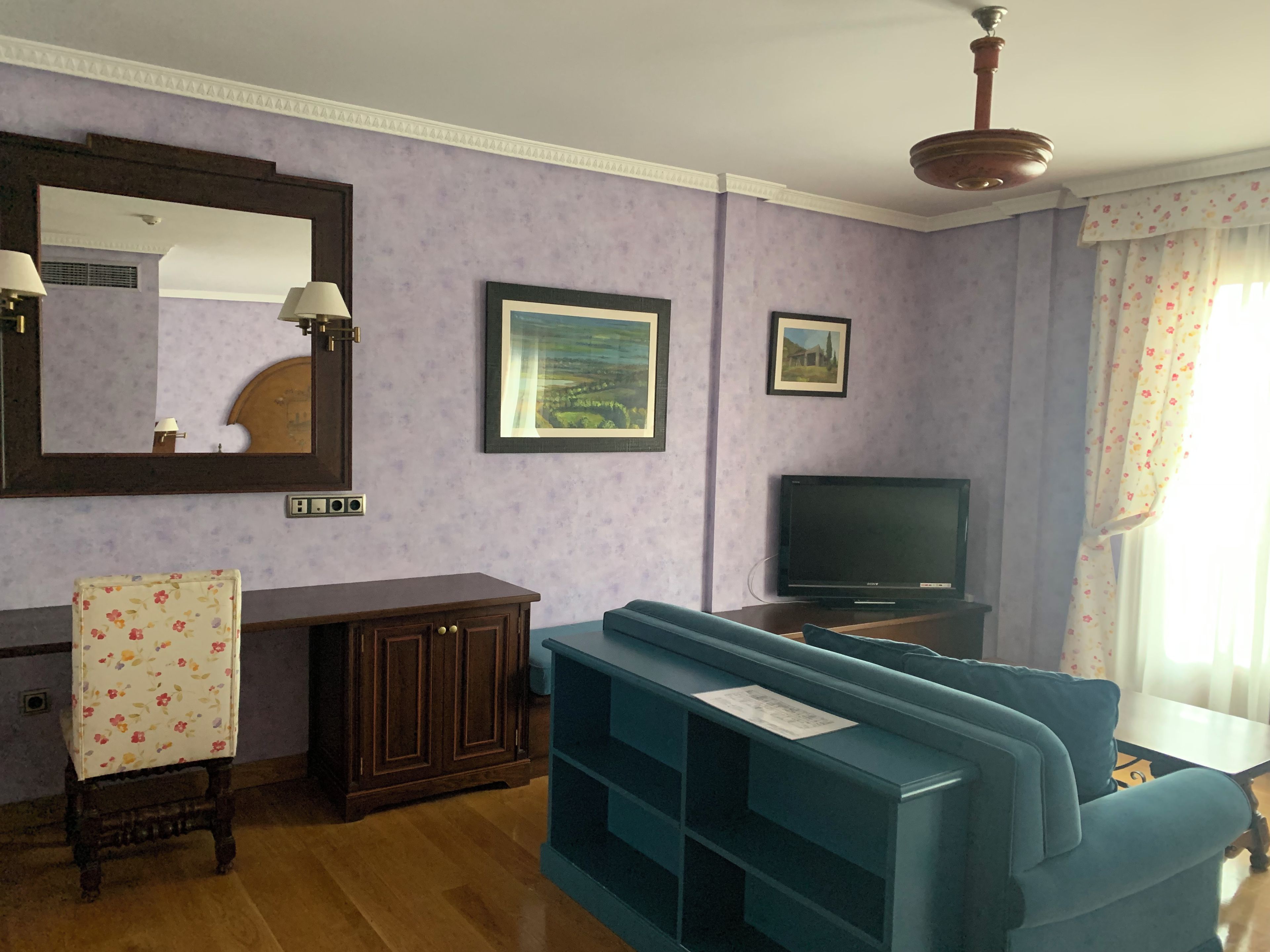 Ein Wohnzimmer mit einem blauen Sofa, einem Fernseher, einer Kommode und einem Spiegel.