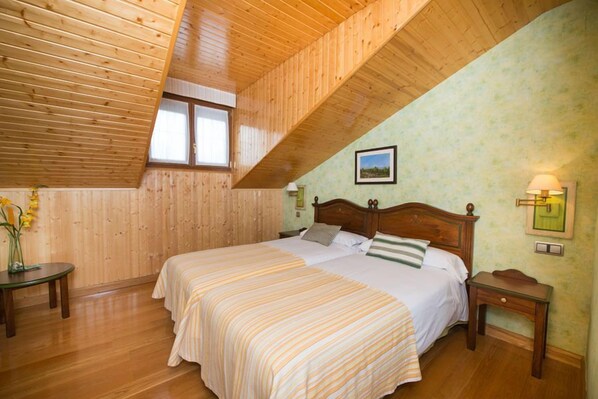 A bedroom with two beds, wooden ceiling, a window, a nightstand, and a wall-mounted lamp. - Hospederia La Canada (Moralzarzal)