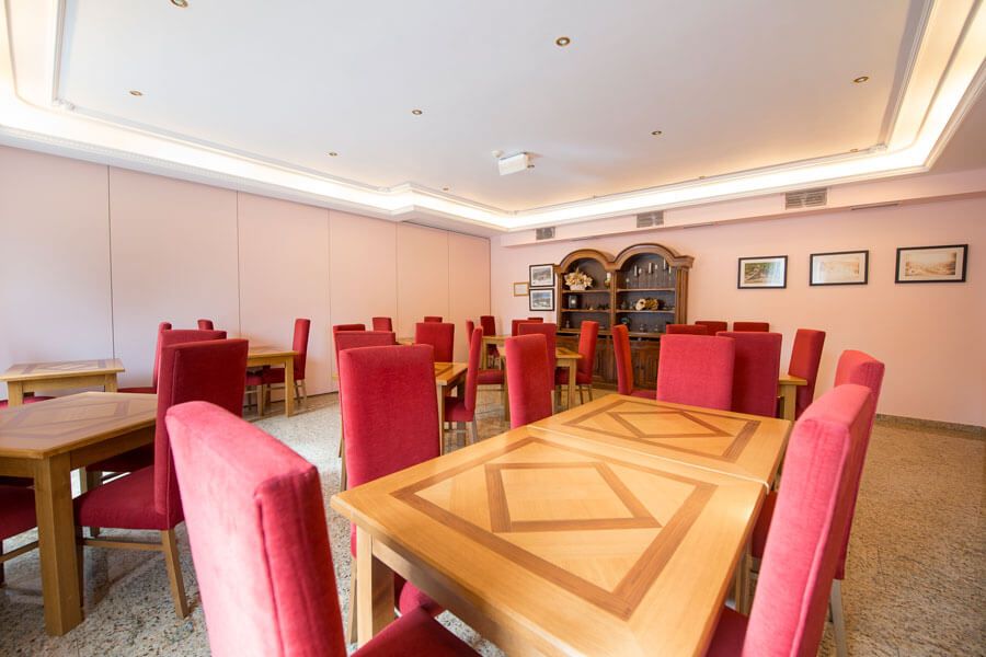 Une salle de conférence avec une longue table et des chaises rouges, un buffet en bois orné de tableaux encadrés et un plafond doté d’un éclairage encastré.