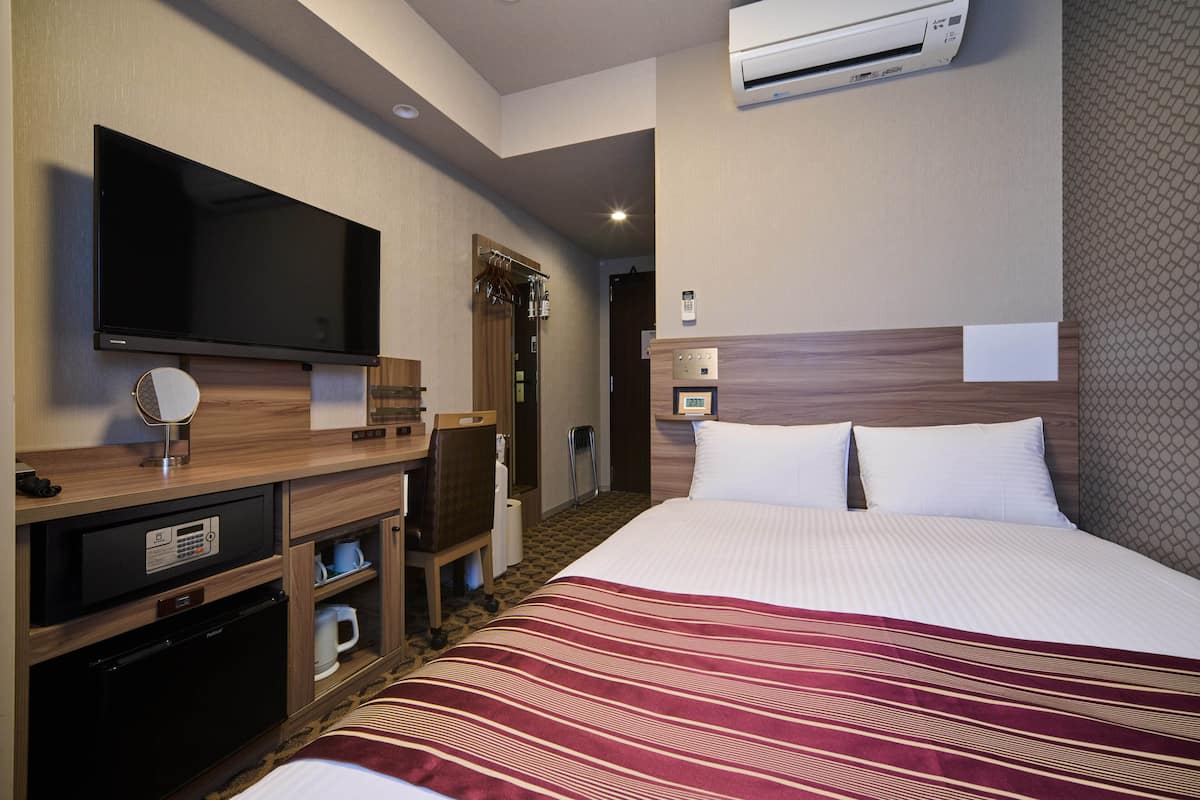 Habitació d'hotel amb un llit, una televisió, una escriptori amb una màquina de cafè i un armari.