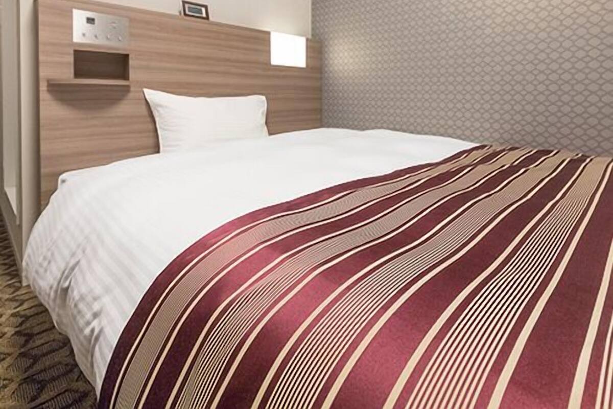 Habitació d'hotel amb un llit, aire condicionat fixat a la paret, una petita estant i un mur amb dibuixos.