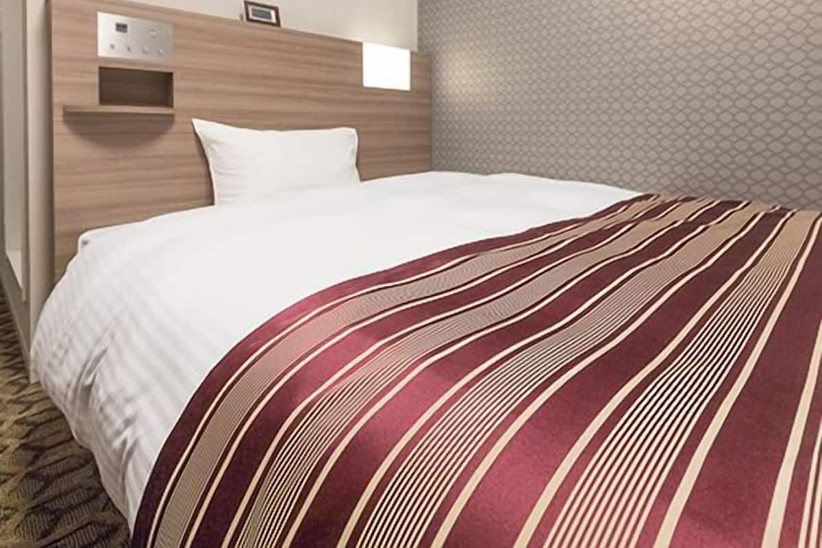 Una habitación de hotel con cama, aire acondicionado de pared, una pequeña repisa y pared decorada.