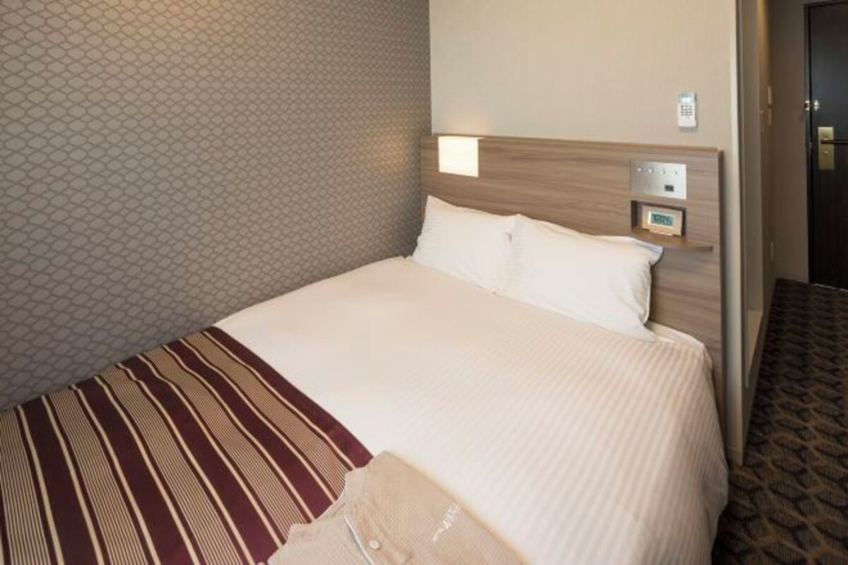 Habitación de hotel con una cama grande, una mesita de noche y un panel de control en la pared.