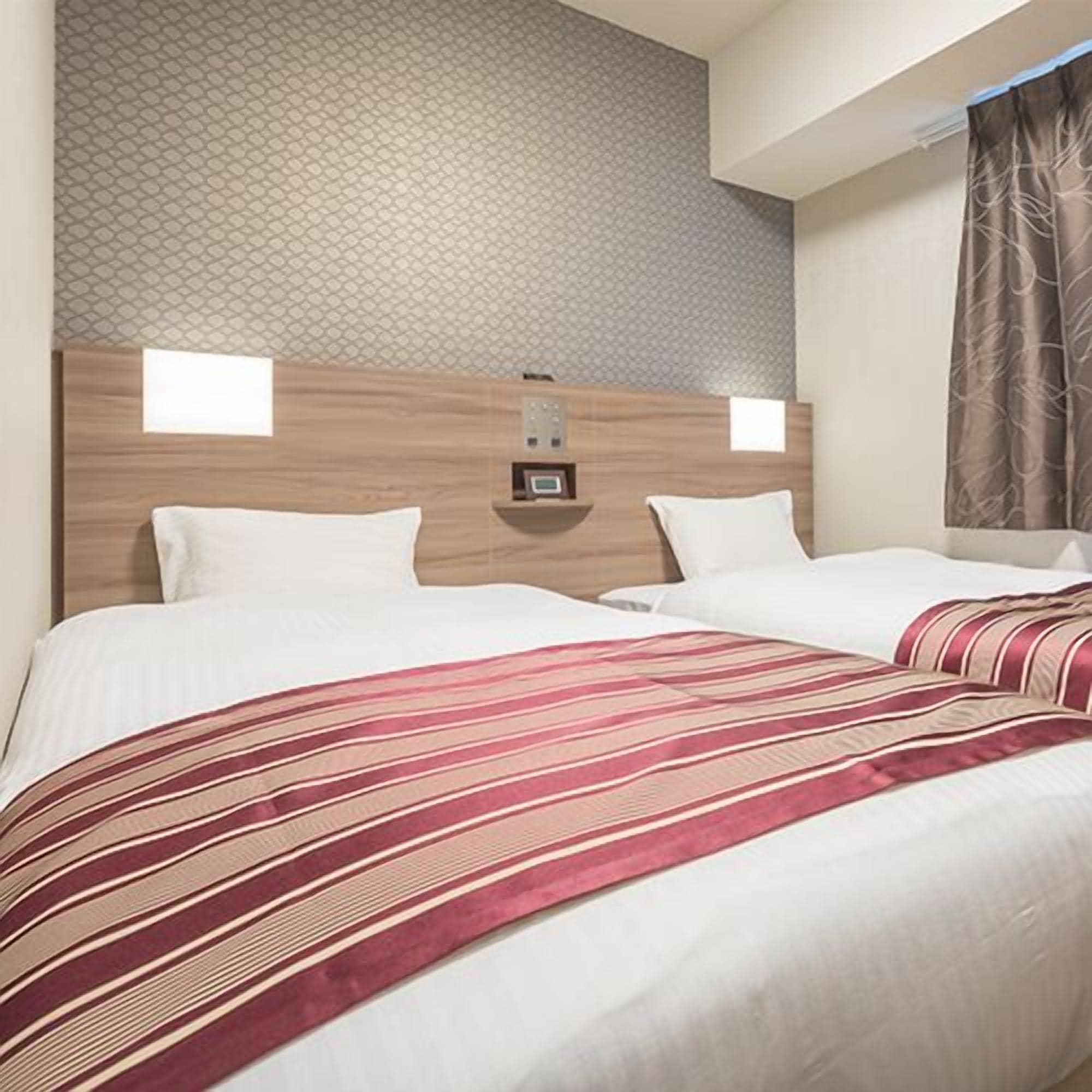 Ett hotellrum med en sänggavel i trä, två vita kuddar, ett randigt överkast och en vägg med mönster.