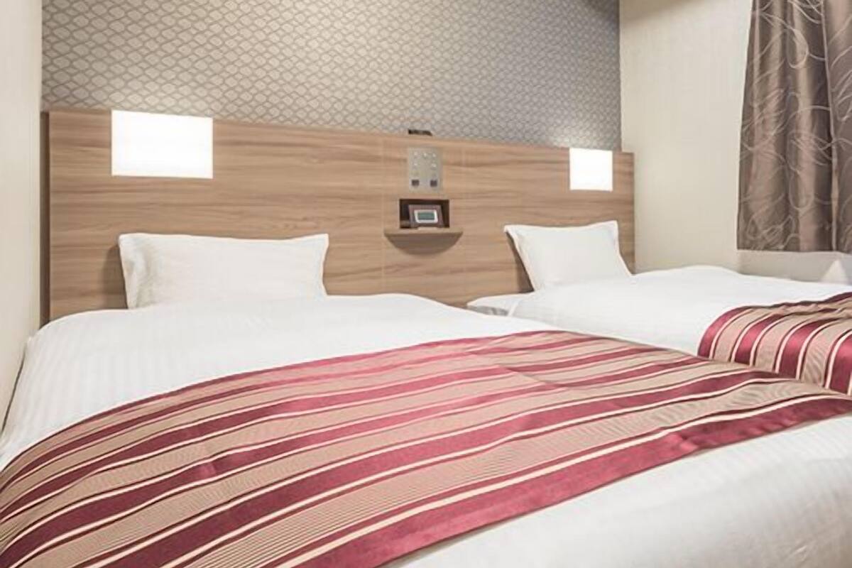 Habitació d'hotel amb un capçal de fusta, dos almoines blanques, un edredó a ratlles i una paret amb dibuixos.