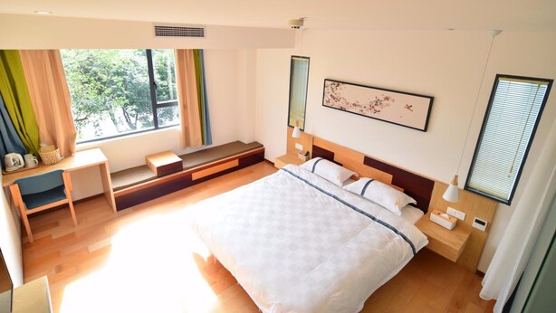 Een moderne slaapkamer met een groot bed, nachtkastje, raam met gordijnen en een klein zithoekje met een bankje en een stoel.
